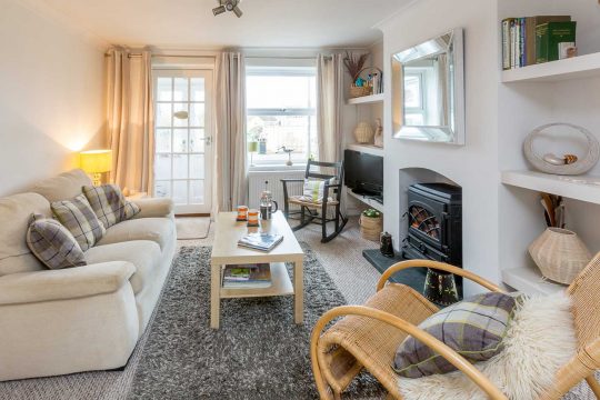 Walnut Cottage, Aldeburgh - sitting room with cream sofa, wood burner and rattan armchair
