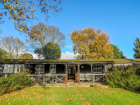 7 Uplands, two bedroom cottage in Thorpeness - black timber bungalow with covered veranda and lawn under autumn trees