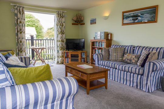 4 Bell Lodge, three bedroom lodge in Thorpeness - living room with blue striped sofas and doors to a balcony