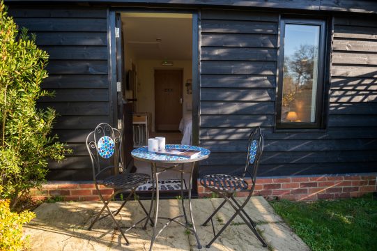 Orford Stables, studio apartment in Benhall - black timber exterior with open door and mosaic bistro table on the patio