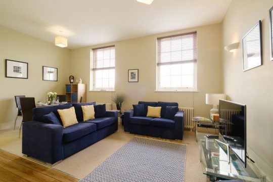 Monarch House, Aldeburgh - living room with two navy sofas, dining table and sash windows