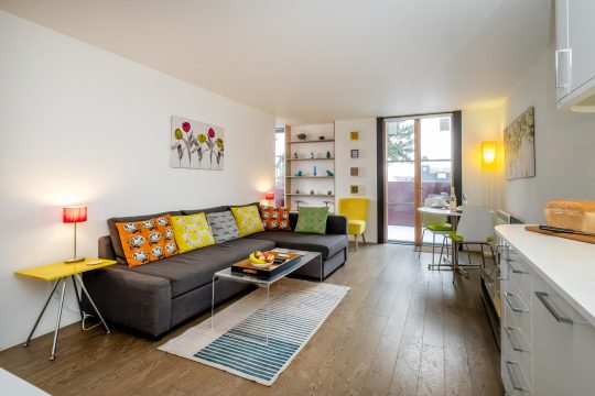 Regatta studio apartment, Thorpeness - living room with corner sofa and doors to the patio