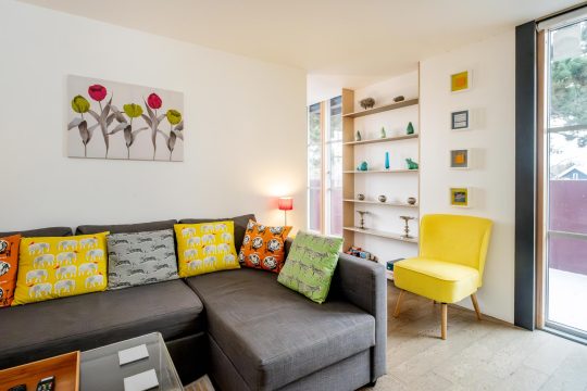 Regatta studio apartment, Thorpeness - corner sofa, shelving and yellow armchair