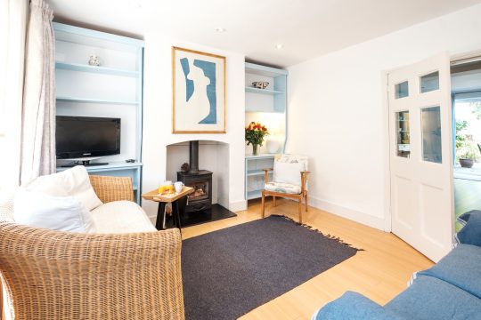 201 High Street, two bedroom cottage in Aldeburgh - living room with wicker sofa, wood burner and blue painted shelving