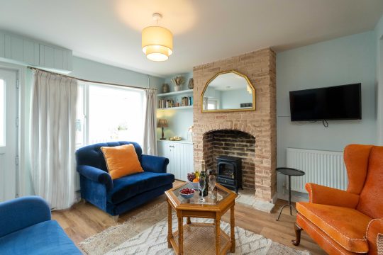 Quay Cottage, two bedroom cottage in Aldeburgh - sitting room with exposed brick fireplace, blue and orange armchairs