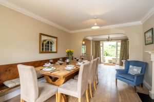 Salt Cellar Cottage, Aldeburgh - dining room with long wooden table, bench seat and blue armchair